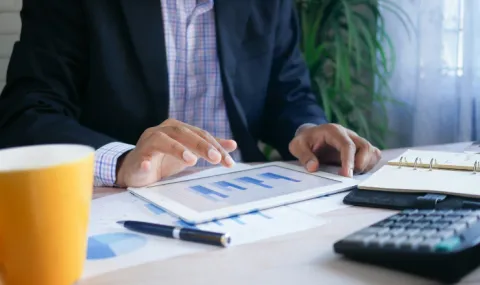 Photo of a person sitting at a desk looking at a tablet with a graph.