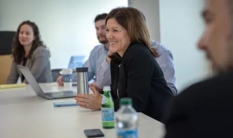 Photo of Catherine Breen at a conference table smiling with hands folded in a meeting.