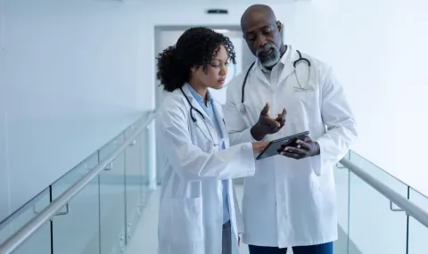 Two health care professionals standing in white coats looking at a tablet. 