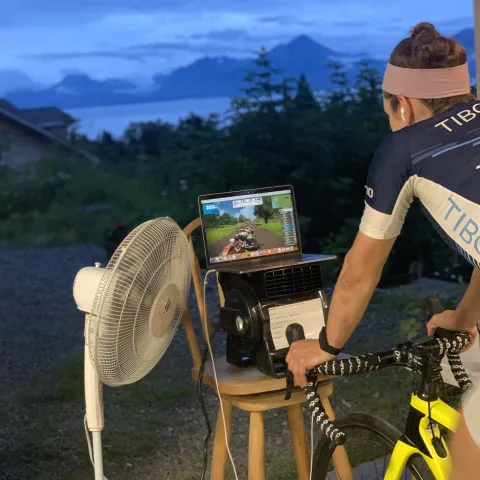 Kristen Faulkner biking outside looking at screen and fan blowing towards her. 