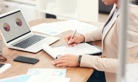 image of woman working at a desk with a laptop reviewing charts.